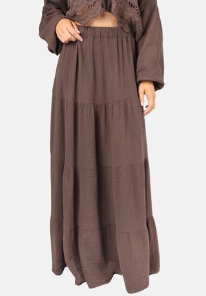 Frau trägt einen braunen gestuften Maxirock mit gerafftem Taillenbund, kombiniert mit einem passenden Langarmoberteil mit Spitzen-Details.