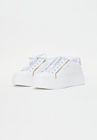 Zapatillas de plataforma blancas con detalles dorados, cordones blancos texturizados y superficie lisa. Destacan por su marca lateral y diseño de puntera redondeada.