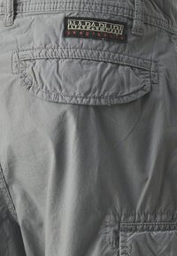 Bermudas cargo de tela gris con superficie texturizada, que cuentan con un gran bolsillo trasero y un parche de logo "Napapijri" en negro y rojo.