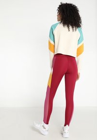 Leggings rossi a vita alta con pannelli laterali colorati in rosa e giallo, abbinati a un maglione corto multi-colore con pois.