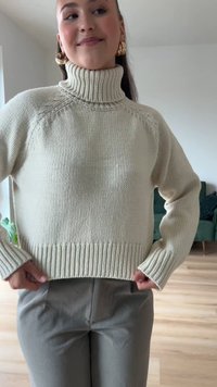 Kreminės spalvos megzta golfiuko tipo palaidinė su banguotomis rankogaliais ir apatine dalimi; derinama su šviesiai pilkais kelnėmis. Minkšta tekstūra ir laisvas kirpimas.