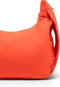 Narancssárga szövet válltáska sima textúrával, ívelt formával és cipzáras záródással. Dombornyomott logó részletekkel ellátva.