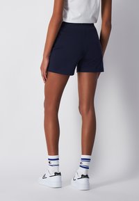 Bermudas de algodón azul marino con cintura elástica, combinadas con zapatillas blancas y calcetines a rayas, mostrando un look atlético y casual.