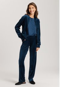 Velour träningsoverall i mörkblått, med en jacka med dragkedja och långa ärmar samt matchande lösa byxor. Slät textur, enkel design.