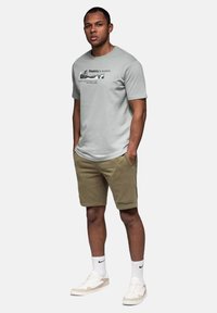 T-shirt gris à col rond avec texte imprimé, associé à des shorts kaki avec poches latérales, porté avec des baskets blanches et des chaussettes mi-mollet.