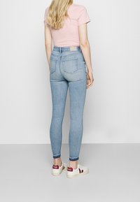 Vaqueros de tiro alto de color azul claro con un corte ajustado, que cuentan con bolsillos traseros y una textura de denim suave; combinados con zapatillas blancas y rojas.