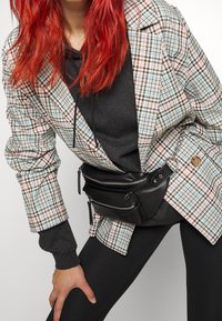 Blazer a cuadros en tonos pastel con acentos en negro, superpuesto a una sudadera oscura y leggings. Presenta una riñonera negra con cremallera.