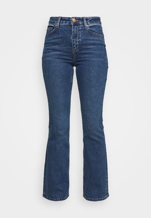 Högmidjade blå jeans tillverkade av denim. Utrustade med utsvängd byxben-design med knappknäppning och fickor. Har en klassisk tvätt och sömdetaljer.