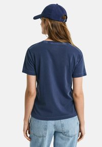 Marineblå bomulds t-shirt med korte �ærmer, med en rund halsudskæring og stikninger. Sammen med lyseblå denim jeans.