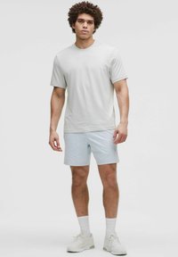 Svetlosivý krátky rukáv T-shirt s okrúhlym výstrihom, v kombinácii so svetlomodrými šortkami. Oblečenie má voľný strih a hladkú textúru.