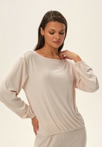 Jasnobeżowa bluzka z długim rękawem o luźnym kroju i prążkowanej teksturze, z szerokim dekoltem w kształcie łódki oraz elastycznymi mankietami.