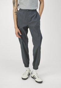 Jogging gris en tissu léger. Présente une taille élastique, des poches latérales et des poignets resserrés aux chevilles.