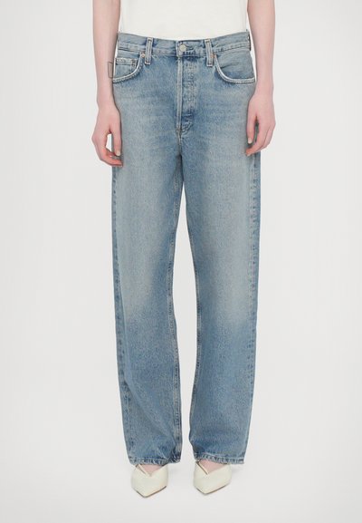 Jeans a gamba larga in denim azzurro chiaro con vita alta, design classico a cinque tasche e leggera scoloritura. Abbinati a scarpe a punta di colore bianco sporco.