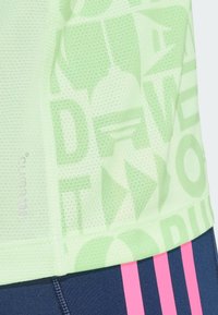 Svijetlozeleni mrežasti atletski top s teksturiranim uzorkom slova i oblika, s crno-ružičastim prugastim dizajnom na donjem rubu.