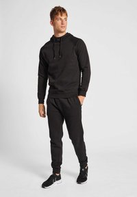 Sort sports hoodie med snor og ribbede mansjetter, parret med matchende sweatpants. Slank design og stoftekstur, båret med sorte sneakers.