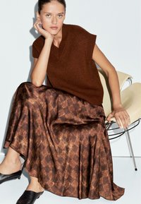 Top sans manches en tricot marron associé à une longue jupe à motifs avec un design en losange dans des tons chauds. Texture lisse et style minimal.