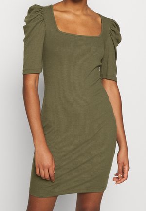 Close-up van een persoon die een olijfgroene geribbelde jurk draagt met pofmouwtjes en een vierkante halslijn.