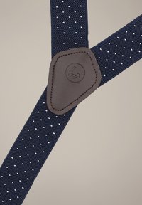 Granatowe szelki o fakturowanej powierzchni z białymi kropkami, uzupełnione brązowym skórzanym akcentem z okrągłym logo.