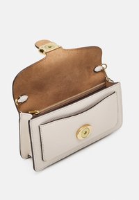 Monedero de cuero beige claro con un cierre circular dorado, interior de ante, compartimento con cremallera y un bolsillo en la parte frontal.