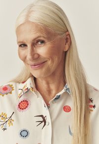 Valge särgi nööpidega ees, mis on kaunilt tikitud erksate lillemotiividega, sealhulgas punase, kollase ja sinise mustriga, ning särgil on sile kangapind.