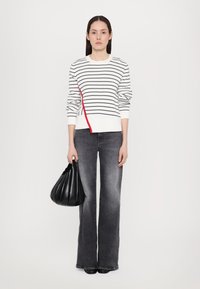 Pulover stripe alb și bleumarin cu un accent roșu, combinat cu blugi gri evazați și o geantă de piele neagră cu un design plisat.
