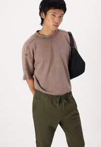 Barna, oversized póló, raglánujjakkal és varrott díszítésekkel, olíva zöld, elasztikus derékpántos nadrággal párosítva, amely oldzsebekkel rendelkezik.