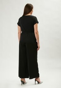 Completo due pezzi nero composto da una maglietta a maniche corte e pantaloni a gamba larga. Realizzato in tessuto morbido, impreziosito da una vita cinchata.