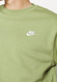 Vaaleanvihreä svetari pehmeästä kankaasta, jossa on pyöreä pääntie ja pieni valkoinen Nike-logo rinnassa.