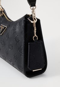 Borsa a mano sintetica nera con texture, hardware dorato, accento con logo e un charm rimovibile. Chiusura con zip e dettaglio della tracolla regolabile.