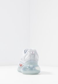 Vitaid sko i vitt med ett överdel av mesh, genomskinlig sula och röda detaljer. Har en texturerad design och reflekterande element på hälen.
