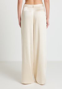 Hosen mit weitem Bein aus einem weichen, cremefarbenen Stoff; zeichnen sich durch eine glatte Textur, zwei Gesäßtaschen und einen taillierten Bund mit Gürtelschlaufen aus.