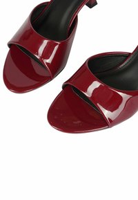 Sandali con tacco in pelle rossa lucida, con punta aperta e ampia fascetta curva sopra il piede. Presentano un tacco piccolo e quadrato.