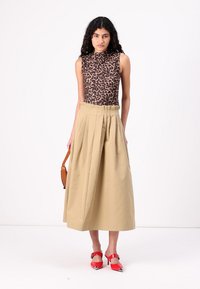 Leopard print sleeveless top, high neckline, beige pleated midi skirt, red heeled shoes, and a brown crossbody bag.
