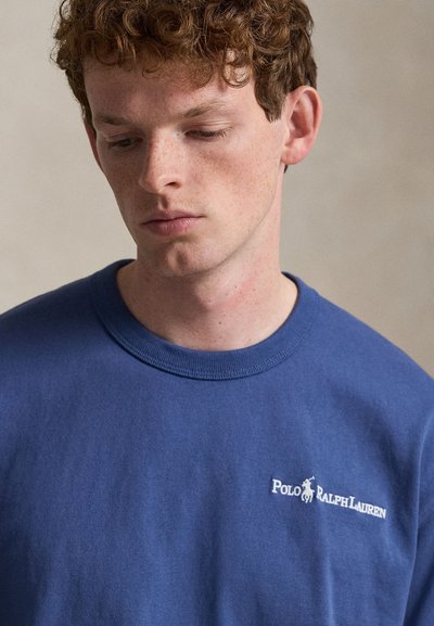 Μπλε βαμβακερό μπλουζάκι με στρογγυλή λαιμόκοψη και κοντά μανίκια. Διαθέτει λευκό λογότυπο "Polo Ralph Lauren" στην αριστερή πλευρά του στήθους.