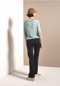 Light blue long-sleeve top, black pants, yellow sneakers, and a brown cap. Smooth texture with minimalist design. Rear view against a neutral backdrop.