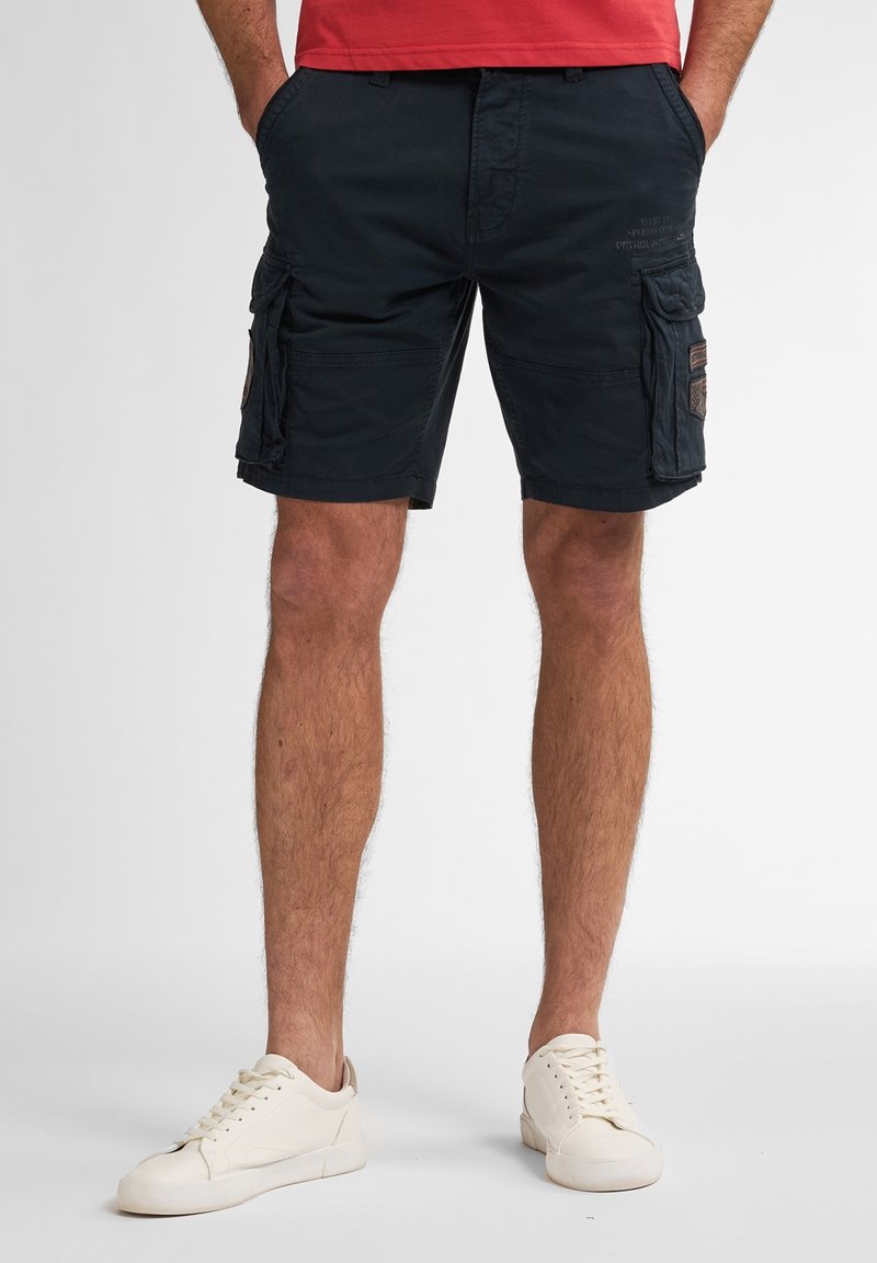 Marine cargo shorts met meerdere zijzakken, een ontspannen pasvorm, en een stevige katoenmix stof. Gecombineerd met witte sneakers.