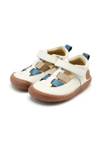Sandalias de cuero blancas con acentos trenzados en azul y beige, correa de velcro, suela de goma marrón y pequeña pestaña de tacón azul. Forma redondeada.