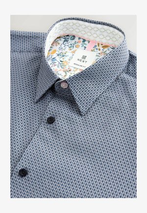 Camicia blu con motivo a fantasia, realizzata in tessuto testurizzato, con una stampa floreale all'interno del colletto. Due bottoni in plastica nera e rosa. Etichetta del marchio visibile.