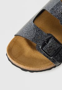 Μαύρο σανδάλι με γλιστρητό σχέδιο με δύο ρυθμιζόμενα λουράκια, καφέ σουέτ εσωτερική σόλα και υφασμένο μαύρο καουτσούκ εξωτερική σόλα.