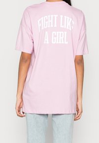 T-shirt in cotone rosa con maniche corte e una vestibilità comoda. Sul retro c'è il testo "FIGHT LIKE A GIRL" in lettere bianche in grassetto.