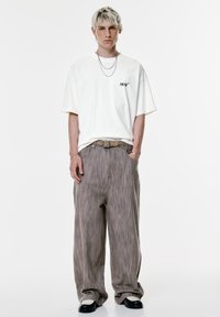Hvid t-shirt med korte ærmer, hvor "1978" er trykt i sort, parret med løstsiddende bukser med brune striber og sort-hvide sko.
