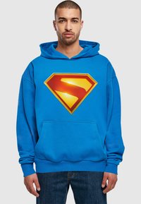 Blue hoodie made of soft fabric, featuring a large yellow and red Superman logo on the front, with a kangaroo pocket and drawstring hood.