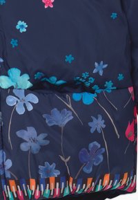 Námořnická puffy bunda s multibarevnými květinovými vzory a živým pruhovaným lemem. Měkký materiál s prošívanou strukturou.