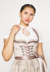 Ελαφρώς κεντημένη φορεσιά με λευκό δαντελωτό μπλουζάκι. Διαθέτει κομμένο κορσέ σε ανοιχτό ροζ και φούστα με λουλουδάτα σχέδια και σατέν κορδέλα.