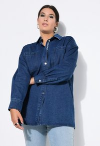 Camicia di jeans di colore blu scuro, con chiusura a bottoni davanti, due tasche sul petto e maniche lunghe con polsini a bottone. Tessuto morbido e vestibilità rilassata.