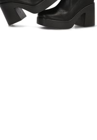 Plataformas negras de tacón hechas de cuero suave, con un tacón rectangular grueso y un diseño de punta redonda.
