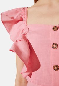 Top in lino rosa con maniche arricciate e bottoni decorativi. Il tessuto presenta una finitura testurizzata con dettagli di cucitura visibili.