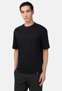 Černé tričko s krátkým rukávem vyrobené z měkké tkaniny, s kulatým výstřihem a malou logovou nášivkou na lemu, spárované s tmavými kalhotami.