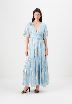 Himmelblaues Maxikleid mit silbernen Blattmustern, tiefem V-Ausschnitt, kurzen, flatternden Ärmeln und gestuftem Rock, kombiniert mit schwarzen SANDLETTEN.