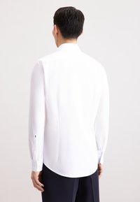 Weißes Langarmhemd mit klassischem Kragen, geknöpften Manschetten und glatter Textur. Verfügt über einen abgerundeten Saum und minimalistische Designelemente.